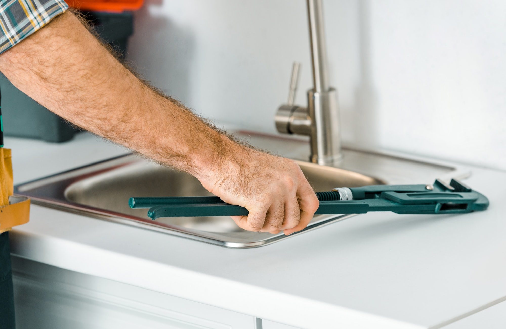 cropped image of plumber holding monkey wrench near sink in kitchen